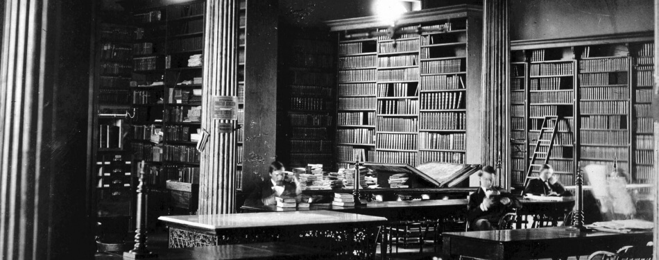 A old black and white image of the library with books to the ceiling and tall columns.