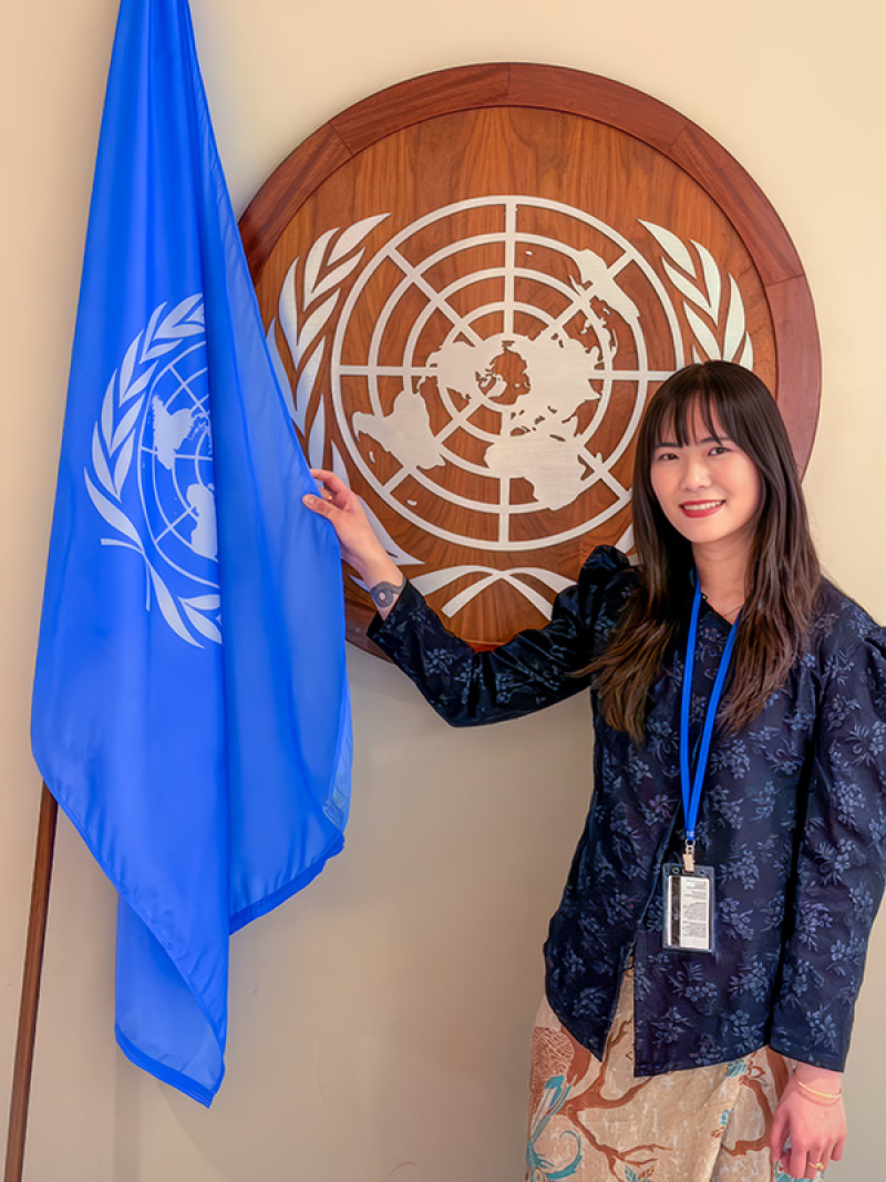 Portrait of Debora Gunawan at the UN Commission on the Status of Women holding a United Nations flag.