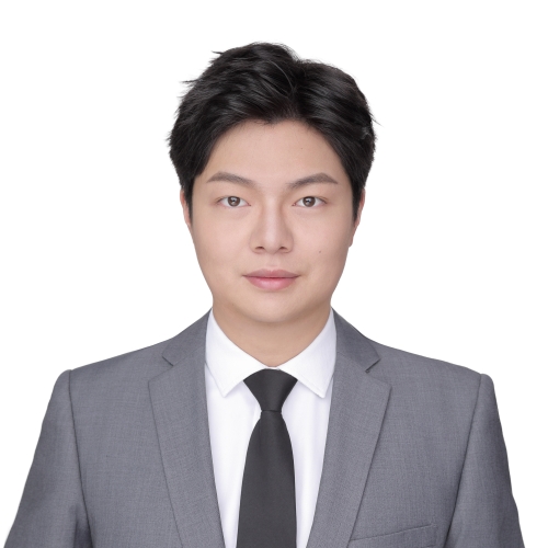 A person in a conservative suit stands in front of a blank background.