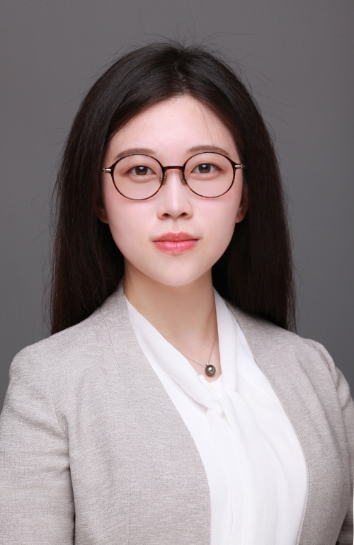 A person with long dark hair and glasses in a neutral blazer and shirt.