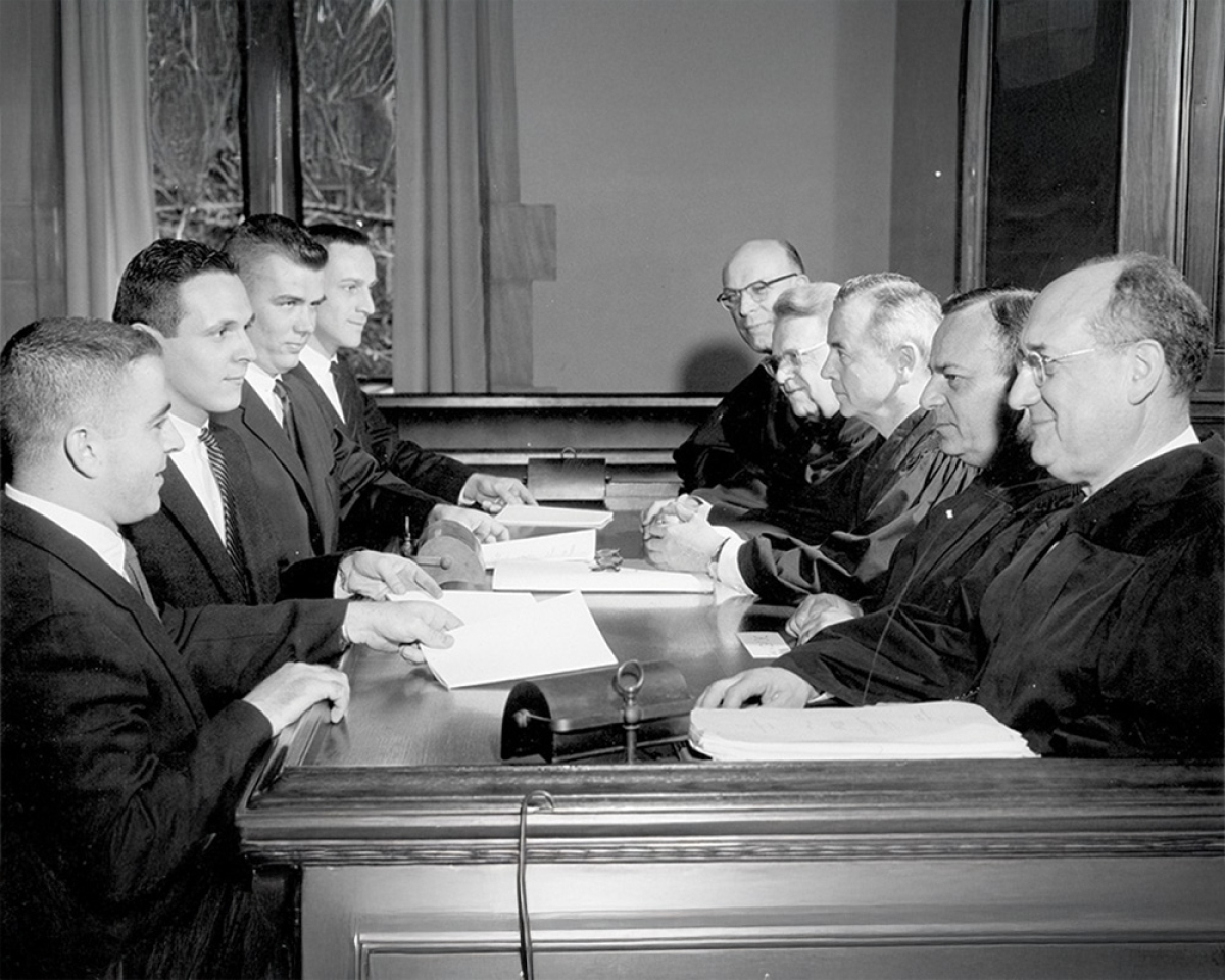 A row of law students in suits face a seated row of judges behind a bench.