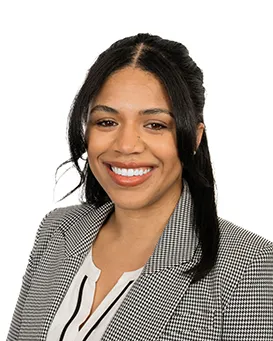 A person with shoulder-length hair and a blazer smiles in front of a white background.
