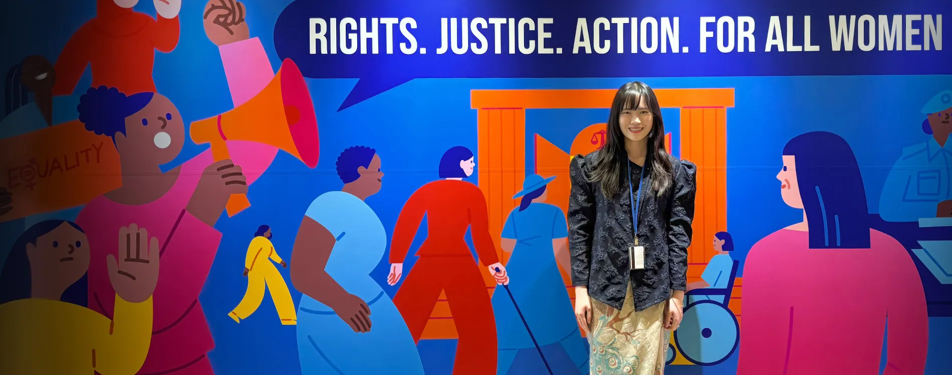 Portrait of Debora Gunawan at the UN Commission on the Status of Women mural that reads Rights. Justice. Action. For All Women.