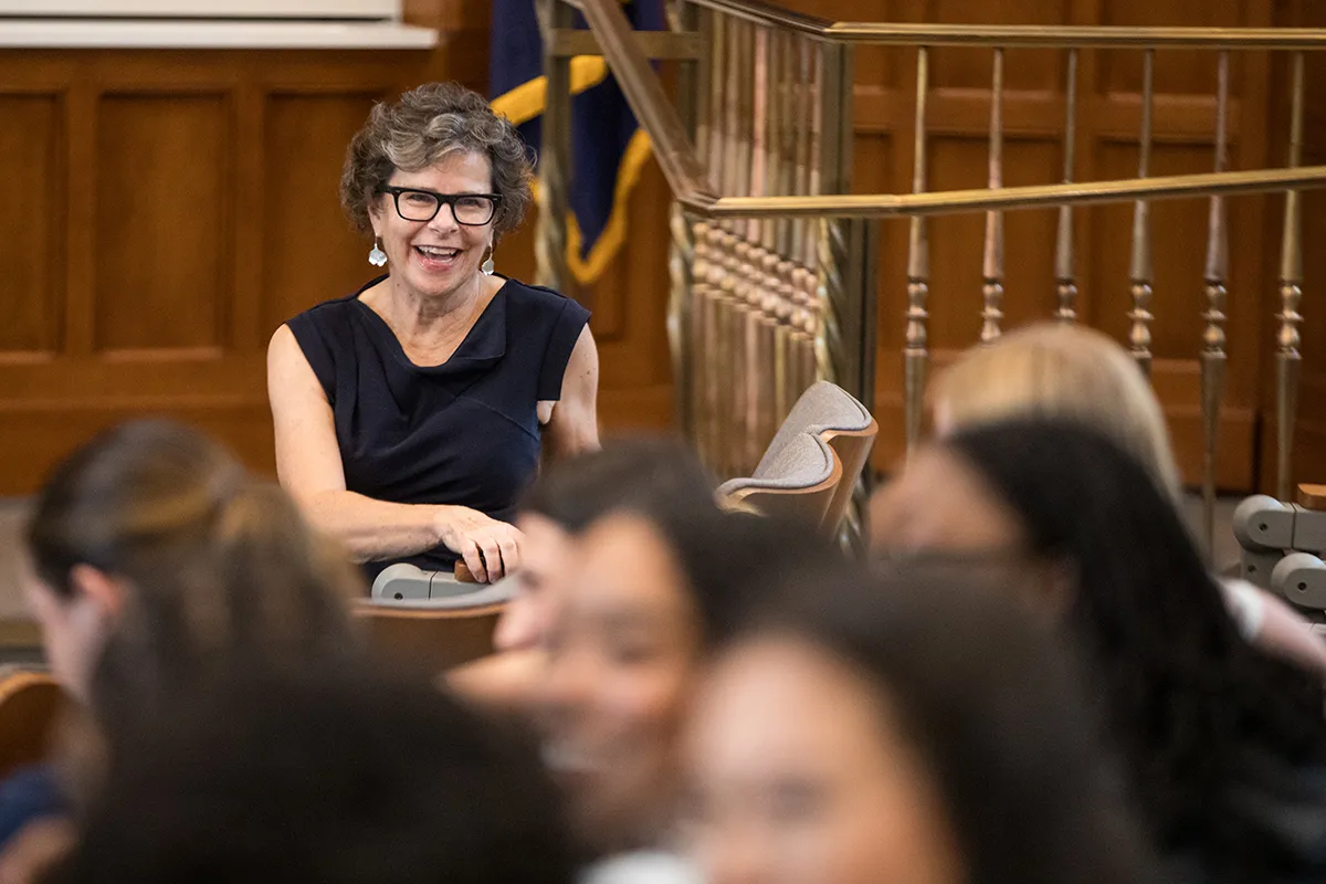 A woman with dark hair smiles and laughs in front of a room of law students.