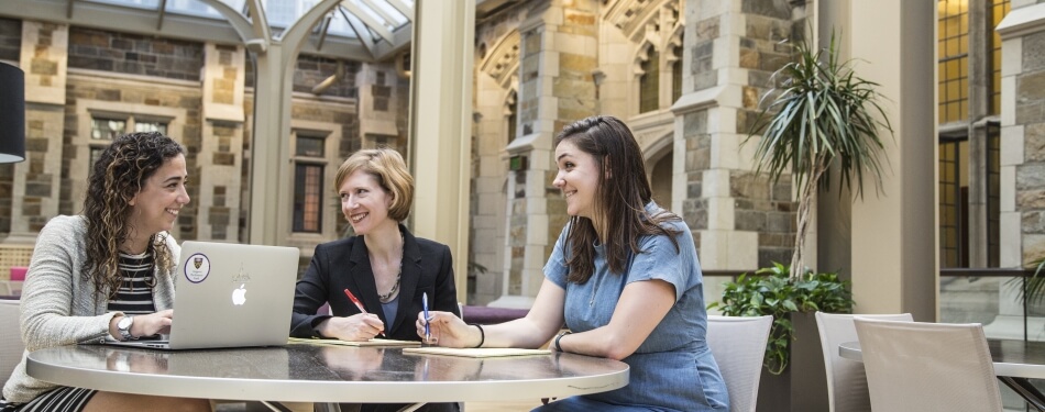 two students sat at a table talking to faculty staff in an atrium setting
