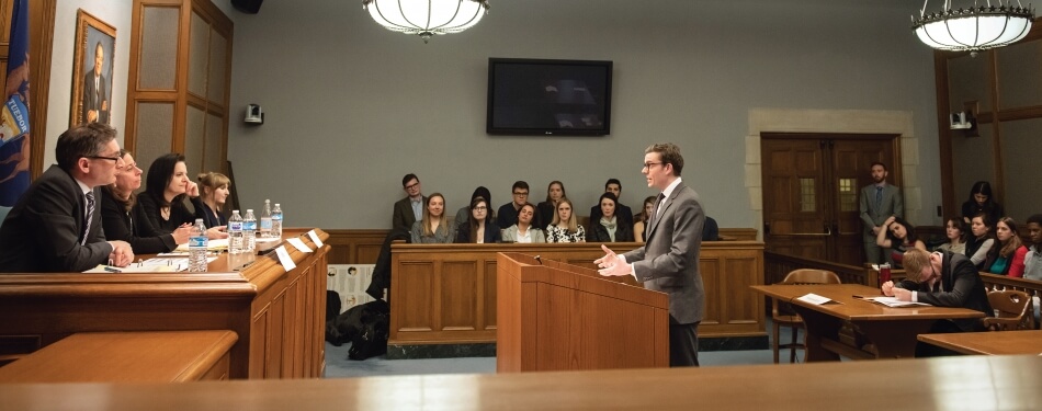 Student arguing at the podium in front of judges in the Court Room classroom.