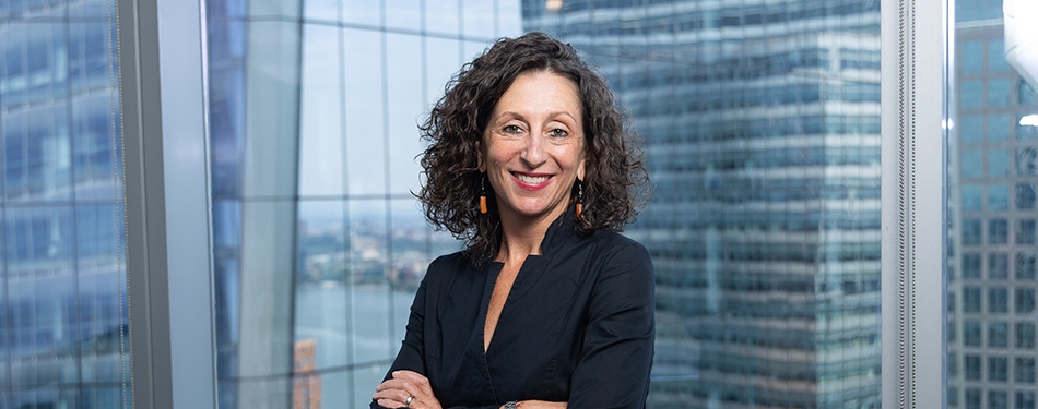 Professor Chavi Nana standing in front a glass wall with city buildings behind her.