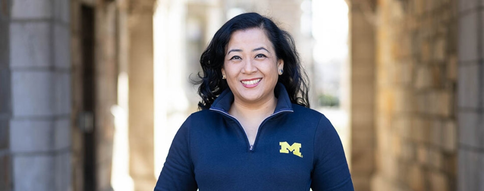 A woman in a Michigan pullover stands under the arches in the Law Quad.