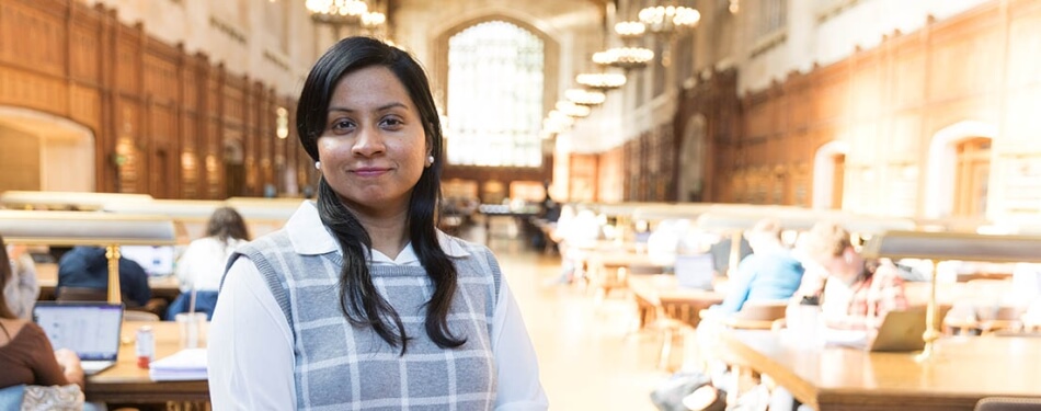 A woman in a sweater vest stands in the Law School Reading Room.