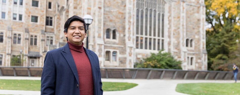 A man in a blazer and turtleneck stands in the Law Quad.