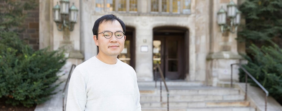 A man in a sweater and glasses stands in front of the doors to Hutchins Hall.