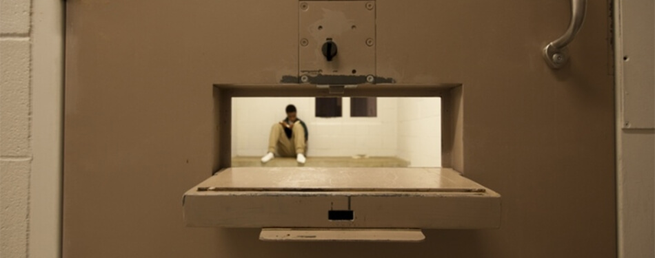 Looking though the food pass door of a jail cell with an inmate sitting on the floor.