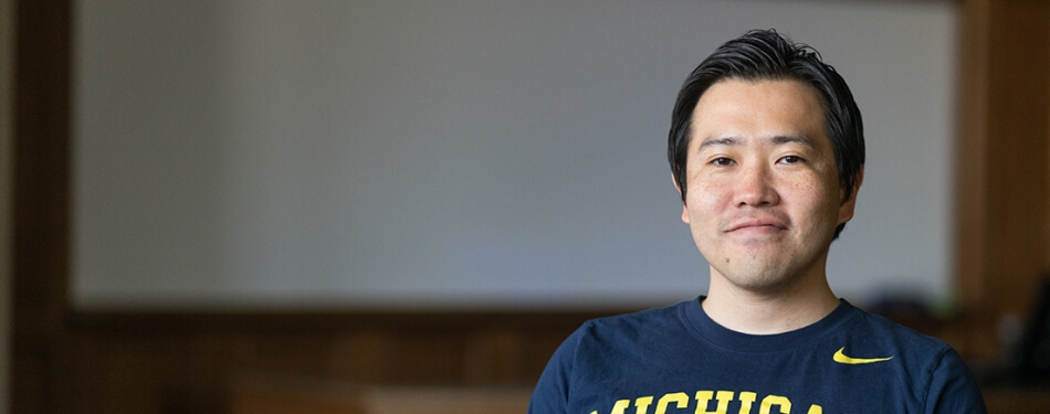 A person in a Michigan Law shirt stands in front of a classroom markerboard.