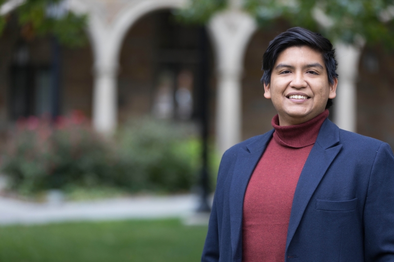 A man in a blazer and turtleneck stands in the Law Quad.