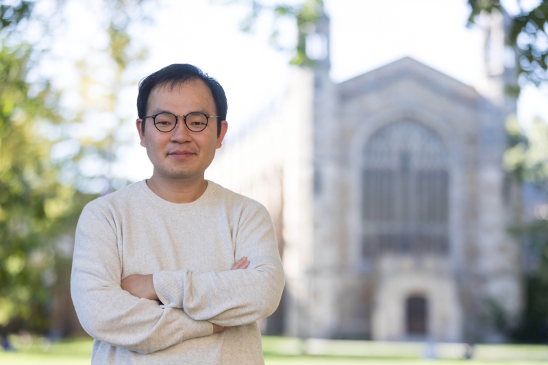 A man in a sweater and glasses stands in the Law Quad.