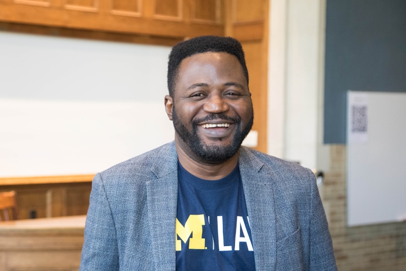 Rotimi Adejoorin smiles and leans against a Michigan Law classroom table.
