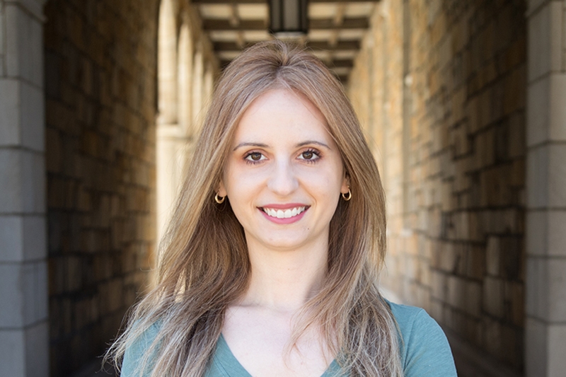 A woman with long hair smiles in a dramatically lit stone corridor.