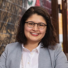 A woman with short hair and glasses smiles in front of a graffit-covered wall.