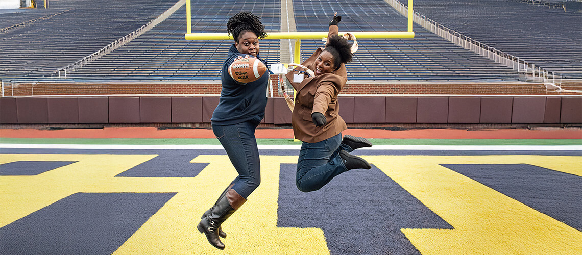 Chioma Nwachukwu and Leticia Kimble jumping on the Michigan Stadium field.