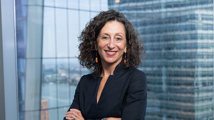 Professor Chavi Nana standing in front a glass wall with city buildings behind her.