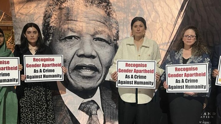 Five people stand in solidarity, holding signs that demand recognition of gender apartheid as a crime against humanity.