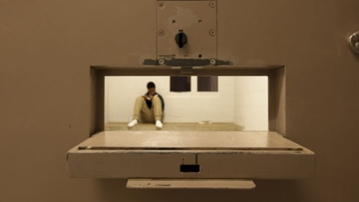 Looking though the food pass door of a jail cell with an inmate sitting on the floor.