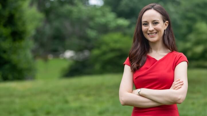 Professor Rachel Rothschild smiling with her arms crossed, standing in a grassy area with trees in the background.