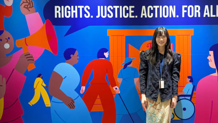 Portrait of Debora Gunawan at the UN Commission on the Status of Women mural that reads Rights. Justice. Action. For All Women.