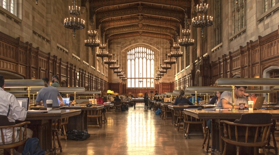 View of the center walkway of a full Reading room where several people are studying.