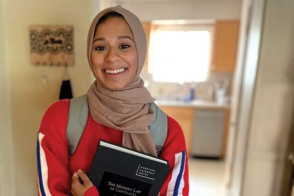 Smiling student holding law book with a backpack on.