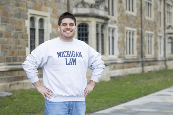 A man stands in the Law Quad in a Michigan Law sweatshirt.