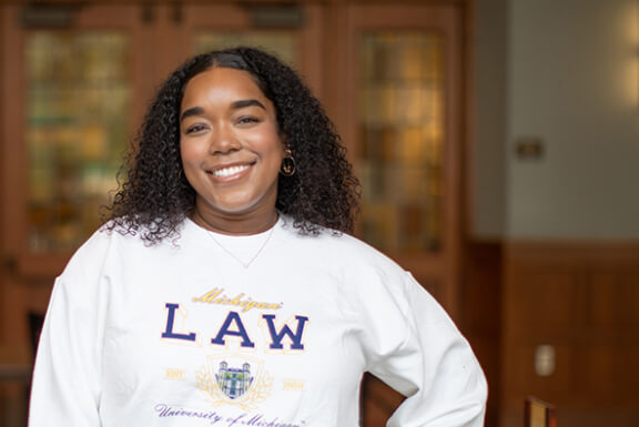 A woman with curly hair smiles in a Michigan Law sweatshirt.