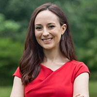 Professor Rachel Rothschild smiling with her arms crossed, standing in a grassy area with trees in the background.